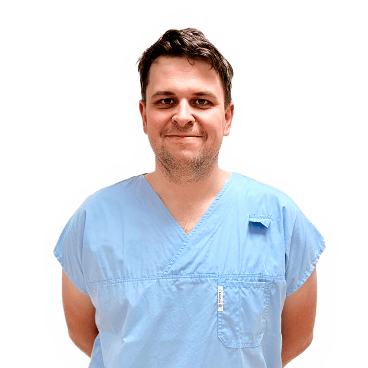 Portrét usmívajícího se muže v modrém lékařském oděvu s krátkými hnědými vlasy na světlém pozadí.